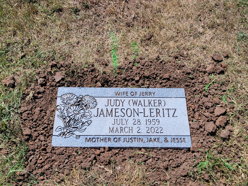 Flat grey granite grave marker carved with daisies, newly set in the ground